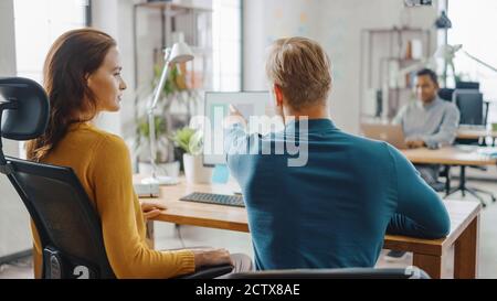 Two Mobile Software Developers Work on Desktop Computer, They Discuss Smartphone Application Design. In the Background Modern Stylish Office with Stock Photo
