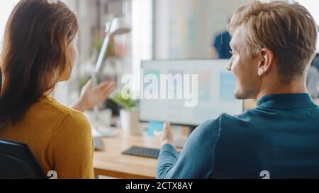 Two Mobile Software Developers Work on Desktop Computer, They Discuss Smartphone Application Design. In the Background Modern Stylish Office with Stock Photo