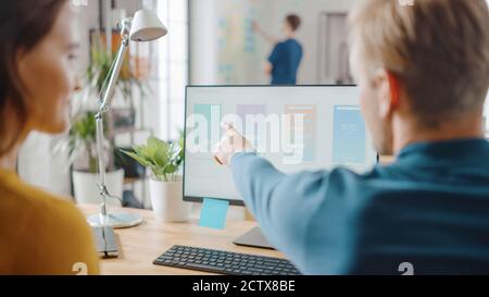 Two Mobile Software Developers Work on Desktop Computer, They Discuss Smartphone Application Design. In the Background Modern Stylish Office with Stock Photo