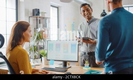 Three Mobile Software Developers Work on Desktop Computer, They Discuss Smartphone Application Design Use Touch Screen Digital Tablet. Modern Stylish Stock Photo