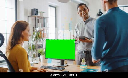 Three Start-up Entrepreneurs Work on Desktop Computer with Green Mock-up Screen, They Discuss Project Design, Use Touch Screen Digital Tablet. Modern Stock Photo
