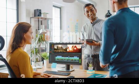 Handsome Male Art Director Consults Beautiful Woman Videographer. Three Beautiful Video Editors Colleagues Discuss Video Project. They Work in a Cool Stock Photo