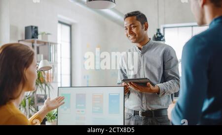 Three Mobile Software Developers Work on Desktop Computer, They Discuss Smartphone Application Design Use Touch Screen Digital Tablet. Modern Stylish Stock Photo