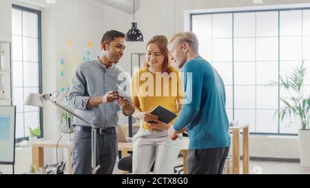 In the Office: Three Diverse Start-up Entrepreneurs Have Meeting and Discussion about the Project. Share Touch Screen Digital Tablet and Smartphone Stock Photo