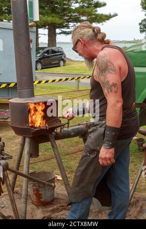 A blacksmith working outdoors at a small forge. Photographed at a travelling fair in Tauranga, New Zealand, February 14 2020 Stock Photo