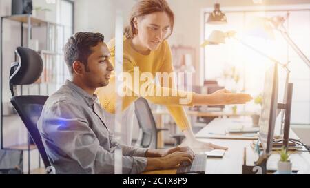 Indian Professional Sitting at His Desk Working on Laptop Computer, Young Beautiful Team Leader Gives Advice about Project Details. Office where Stock Photo