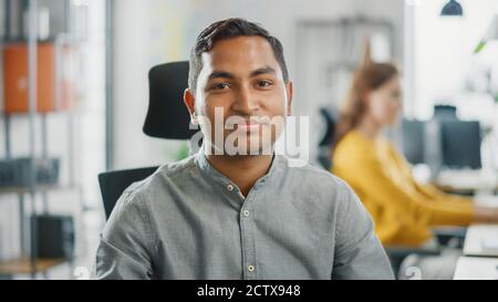 Portrait of Handsome Professional Indian Man Working at His Desk, Using Personal Computer and Smiling at the Camera. Successful Man Working in Bright Stock Photo