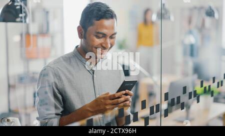 Portrait of Handsome Professional Indian Man Uses Mobile Phone, Writes Important Email, Smiles Charmingly. Successful Man Using Smartphone Working in Stock Photo