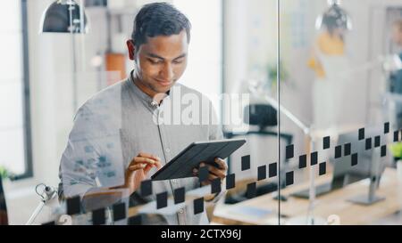 Portrait of Handsome Professional Indian Man Uses Touch Screen Digital Tablet Computer, Writes Important Email, Smiles Charmingly. Successful Man Stock Photo