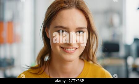 Portrait of Beautiful Young Woman with Red Hair Wearing Yellow Sweater Looking Up to the Camera and Smiling Charmingly. Successful Woman Working in Stock Photo