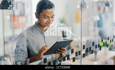 Portrait of Handsome Professional Indian Man Uses Touch Screen Digital Tablet Computer, Writes Important Email, Smiles Charmingly. Successful Man Stock Photo