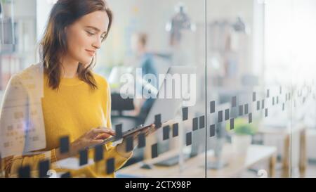 Portrait of Beautiful Young Woman with Red Hair Wearing Yellow Sweater Uses Modern Laptop while Standing. Successful Woman Working in Bright Diverse Stock Photo