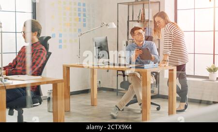Young Professionals Working in Creative Agency in Loft Ofice. Female Colleague Came to Chat to Coworker in Friendly Manner. Diverse Employees. Asking Stock Photo