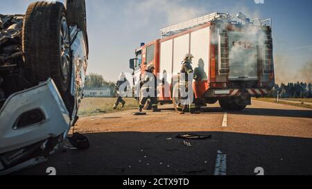 Rescue Team of Firefighters Arrive on the Car Crash Traffic Accident Scene on their Fire Engine. Firemen Grab their Tools, Equipment and, Gear from Stock Photo