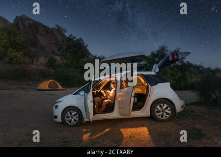 A traveler examines a map while sitting in a car in the mountains under the light of the starry sky. Adventure and travel concept Stock Photo