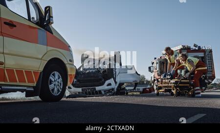 Rescue Team of Firefighters and Paramedics Work on a Terrible Car Crash Traffic Accident Scene. Preparing Equipment, Stretches, First Aid. Saving Stock Photo