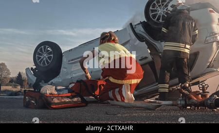 Car Crash Traffic Accident: Paramedics and Firefighters Rescue Passengers Trapped in Burning Rollover Vehicle. Medics Prepare First Aid Tools. Low Stock Photo