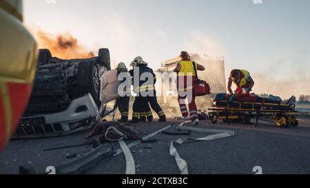 Paramedics and Firefighters Arrive On the Car Crash Traffic Accident Scene. Professionals Rescue Injured Victim Trapped in Rollover Vehicle by Stock Photo