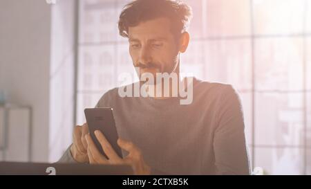 Professional Creative Man Sitting at His Desk in Home Office Studio Using Smartphone, Man Using Mobile Phone, Browsing Through Internet, Social Stock Photo