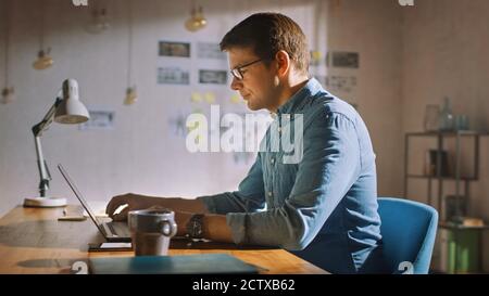 Professional Creative Man Sitting at His Desk in Home Office Studio Working on a Laptop. Man working with Data and Analyzing Statistics. Stock Photo