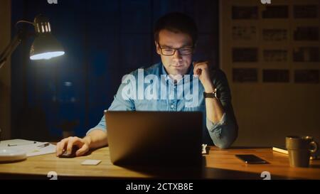 Professional Man Sitting at His Desk in Office Studio Working on a Laptop in the Evening. Man Analyzing Statistics. Stock Photo