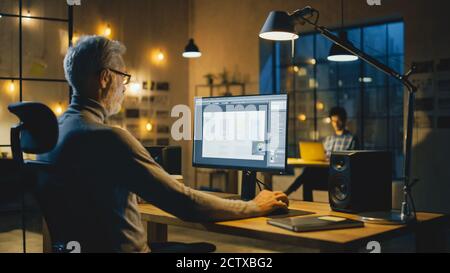 Creative Middle Aged Mobile Software Designer Sitting at His Desk Uses Desktop Computer with Screen Showing Smartphone Application Design Process Stock Photo