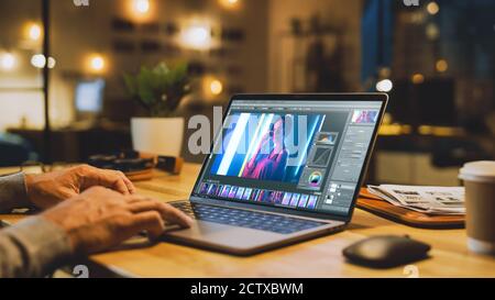 Shot of a Male Digital Editor Specialist Works on a Laptop Computer in Picture Editing Software. In the Backdround Stylish Modern Studio Office in the Stock Photo