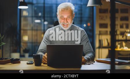 Portrait of the Handsome Smiling Middle Aged Bearded Businessman Working at His Desk Using Laptop Computer. Working from Cozy Home Office Studio with Stock Photo