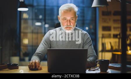 Portrait of the Handsome and Successful Middle Aged Bearded Businessman Working at His Desk Using Laptop Computer. Working from Cozy Home Office Stock Photo