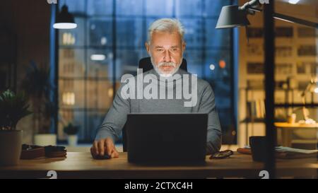 Portrait of the Handsome and Successful Middle Aged Bearded Businessman Working at His Desk Using Laptop Computer. Working from Cozy Home Office Stock Photo