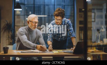 Chief Creative Designer Discusses Design Sheets with Young Developer. Two Professionals Having Discussion, Working with Documents, Choosing Right Stock Photo