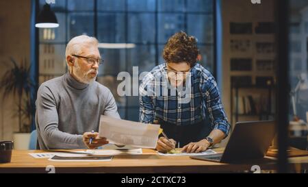 Chief Creative Designer Discusses Design Sheets with Young Developer. Two Professionals Having Discussion, Working with Documents, Choosing Right Stock Photo