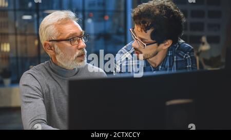 Chief Creative Designer Shows Desktop Computer Screen to a Young Developer, They Discuss Project. Two Professionals Having Discussion. Choosing Right Stock Photo
