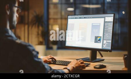 Over the Shoulder Shot of a Young App Developer Using Desktop Computer, Creating New Mobile Phone Application Design, Software UI Development. Evening Stock Photo