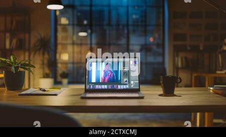 Shot of a Laptop Computer in the Modern Office Showing Photo Editing Software. In the Background Warm Evening Lighting and Open Space Studio with City Stock Photo