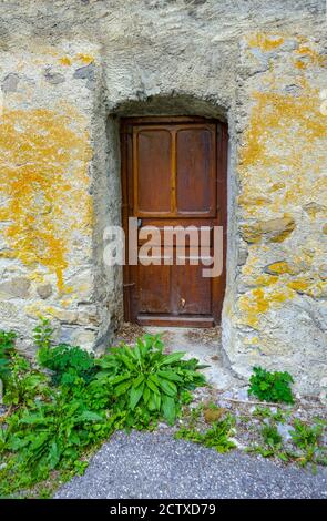 Vegetation in front of wooden doorDoor in old buildings in the village Puy-Saint-Vincent, ski resort, in summer, Vanoise National Park, Ecrins, France Stock Photo