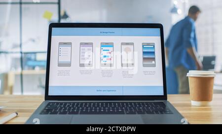 Laptop on the Desk in the Office Shows Screen with Mobile Phone Application Design, Software UI Development. In the Background Creative Modern Open Stock Photo