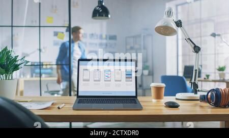 Laptop on the Desk in the Office Shows Screen with Mobile Phone Application Design, Software UI Development. In the Background Creative Modern Open Stock Photo