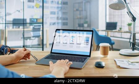 Young Professional Works on a Laptop at His Desk in the Creative Office. Notebook Screen Shows Mobile Phone Application Design, Software UI Stock Photo