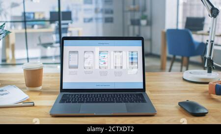 Laptop on the Desk in the Office Shows Screen with Mobile Phone Application Design, Software UI Development. In the Background Creative Modern Open Stock Photo