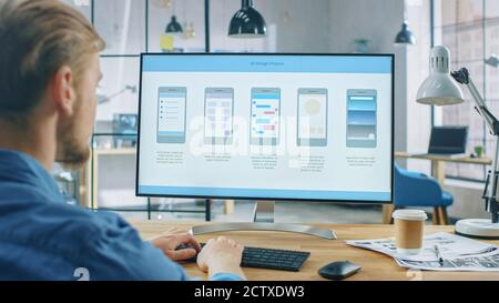 Young Professional Works on Desktop Computer at His Desk in the Creative Office. Monitor Screen Shows Mobile Phone Application Design, Software UI Stock Photo