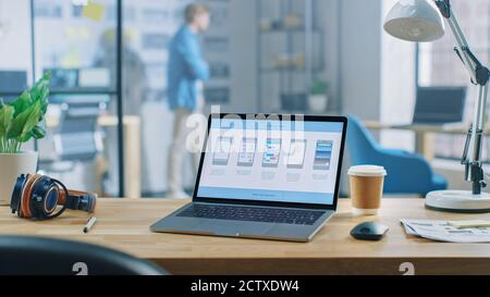 Shot of Laptop Standing at Desk in the Creative Office. Notebook Screen Shows Mobile Phone Application Design, Software UI Development. In Background Stock Photo