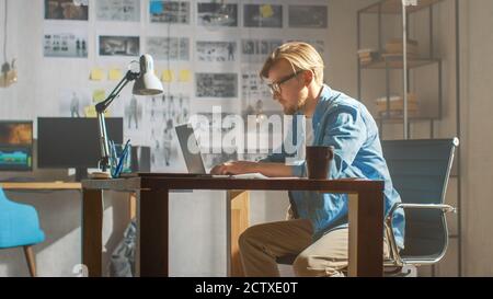 Creative Developer Works on a Laptop in His Studio. Designing Apps, Games and Doing Video Editing. In the Background Modern Sunny Loft Office with Stock Photo