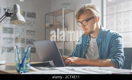 Creative Developer Works on a Laptop in His Studio. Designing Apps, Games and Doing Video Editing. In the Background Modern Sunny Loft Office with Stock Photo