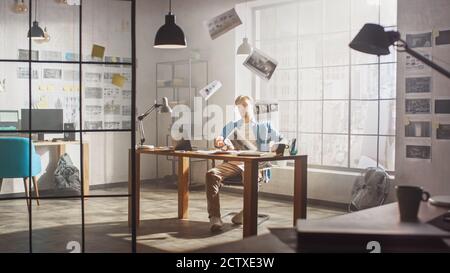 Frustrated and Tired Young Creative Designer Works on Laptop at His Desk, Threw Sheets with Concept Sketches into the Air out of Sheer Despair Stock Photo