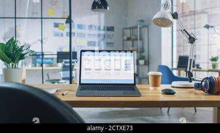 Laptop on the Desk in the Office Shows Screen with Mobile Phone Application Design, Software UI Development. In the Background Creative Modern Open Stock Photo
