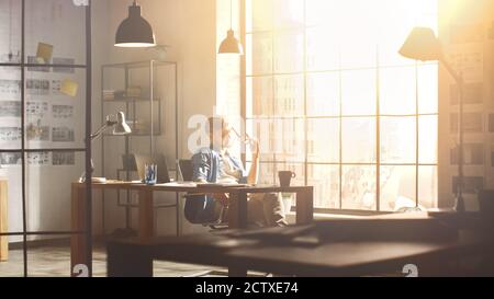 Thoughtful Young Professional Designer Sits at His Desk and Rubs His Glasses, Contemplating Next Steps in Finishing Project. Handsome Professional Stock Photo