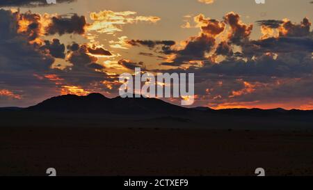 Beautiful majestic sunset with orange and red colors in a partly cloudy sky behind mountains in Namib desert near Sesriem, Namibia, Africa. Stock Photo