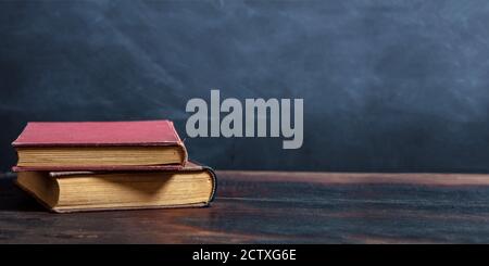 Old books stack on a wooden table, black board background. Library vintage reading desk, template Stock Photo