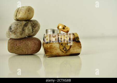 two wedding rings placed on a small chest box near stones stack pile as decoration wedding photography Stock Photo